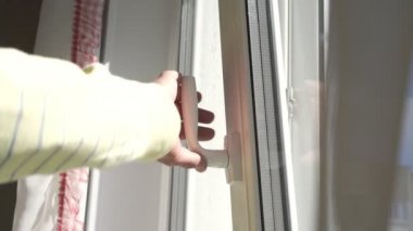 Sarı kazaklı yaşlı adam beyaz plastik pencereyi kapatıyor.