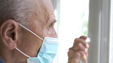 Yüzü buruşuk, mavi maskeli, pencereli emekli.