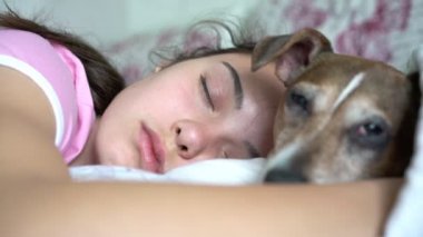 Genç kadın büyük bir yatakta uyuyor ve küçük köpeğe sarılıyor.