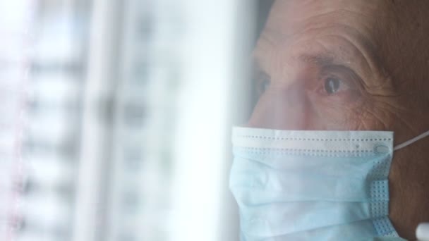Hombre arrugado deprimido en máscara facial azul en la ventana — Vídeo de stock