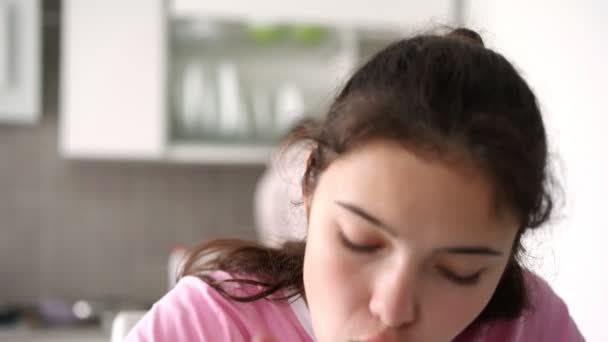 Estudante em rosa come salada de legumes na cozinha falando — Vídeo de Stock