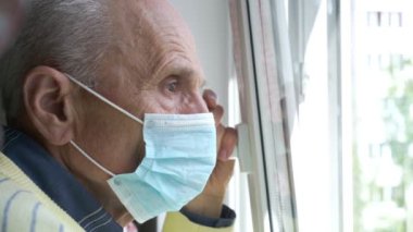 Mavi maskeli buruşuk adam, pencerenin dışındaki ilgiyle bakıyor.