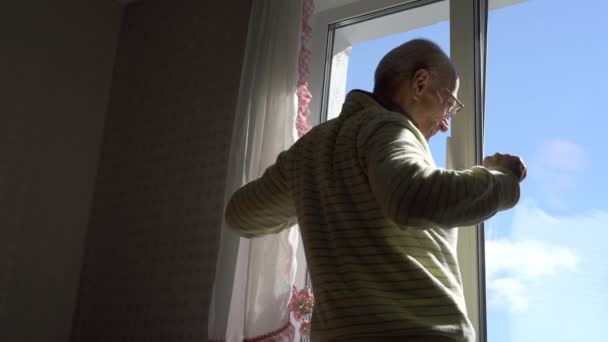 Старший человек стоит у окна и вытягивает тело и руки — стоковое видео