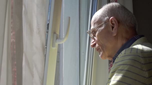 Vieil homme en lunettes regarde à travers la fenêtre en plastique blanc — Video