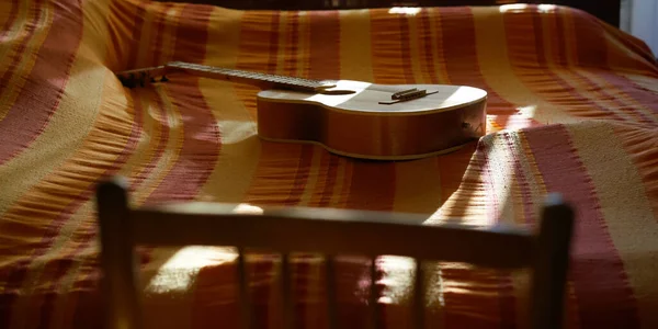 椅背靠在铺有毯子的床上的木制吉他上 — 图库照片