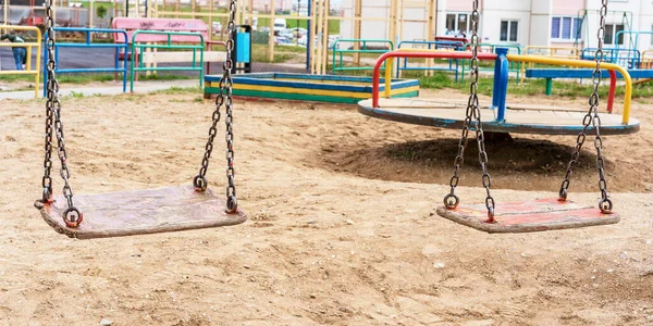 Деревянные качели на ржавых цепях и карусель на детской площадке — стоковое фото