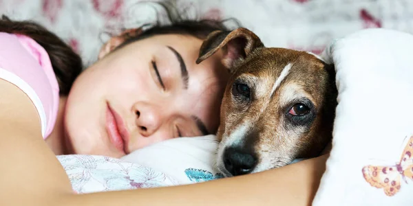 Genç kız yatakta uyuyor ve yavru köpeğe sarılıyor.