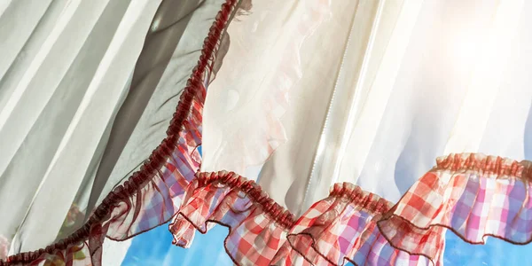 white curtains with red frills against blue sky closeup