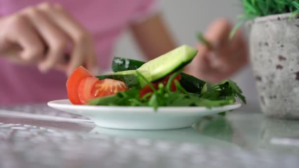 Estudante em camiseta rosa come salada à mesa com planta — Vídeo de Stock