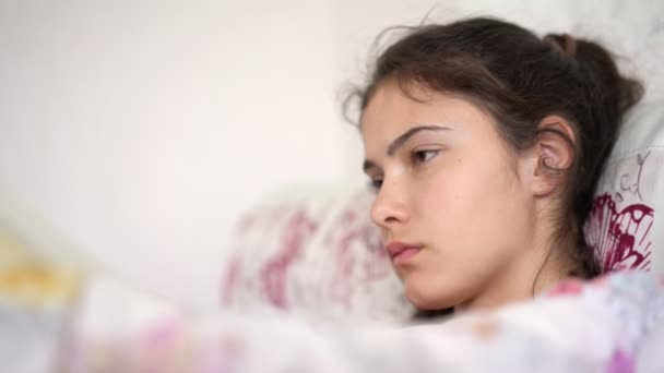 Teenage brunette lies on pillow in bed and reads book — Stock Video