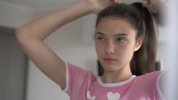Zartes Schulmädchen bürstet lange Haare mit Haarbürste am Spiegel — Stockvideo