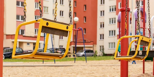 Желтые металлические качели на цепях, расположенных на городской детской площадке — стоковое фото