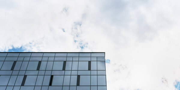 Office building upper levels with large widows against blue sky with dense white clouds at bright sunlight