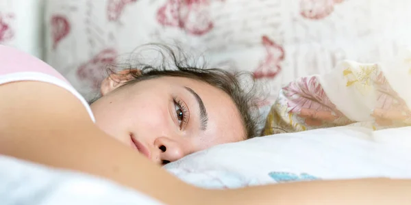 Adolescente chica abre los ojos despertando en la cama con almohadas primer plano — Foto de Stock