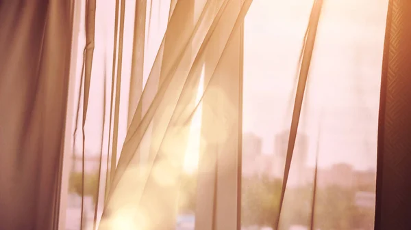 Rüzgâr, bulanık şehir manzarasına karşı oda perdesini kaldırır.