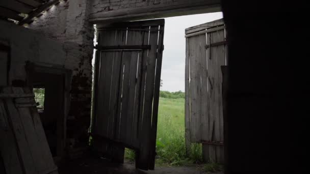 Houten deuren van donker verlaten gebouw tegen weide — Stockvideo