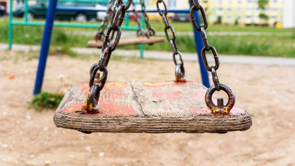 Viejo columpio de madera en cadenas metálicas oxidadas en el patio de recreo local — Foto de Stock