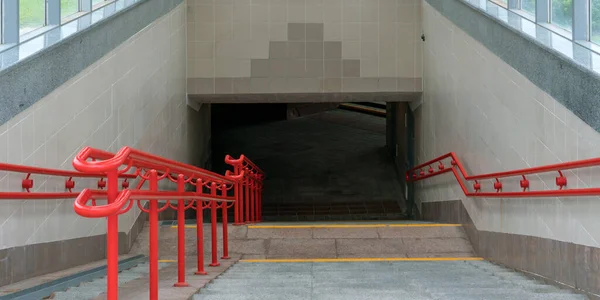 Grå asfalterad trappa till underjordisk gångväg med röda ledstänger — Stockfoto