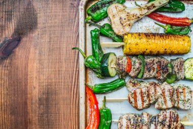 Kızarmış et şişleri, sebzeli ve kavrulmuş mısır kulaklı fırın tepsisi, ahşap arka plan, üst manzara, yazı için yer. Et ve ızgara konsepti