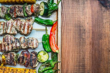 Pişirme tepsisinde sebzeli kızarmış et şişleri ve kırsal ahşap arka plan, üst manzara, yazı için yer. Et ve ızgara konsepti