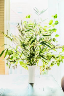 Pencere arkasındaki masada vazoda çok güzel bitkiler var. Çeşitli yeşil tropikal bitkilerle çiçekçi düzenlemeleri. Ev dekorasyonu ve iç mekan, arka plan.