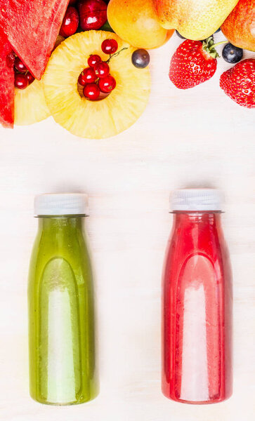 Tasty and healthy summer beverages in bottles with fruits and berries ingredient. Red and green smoothie or juice on white wooden background, top view