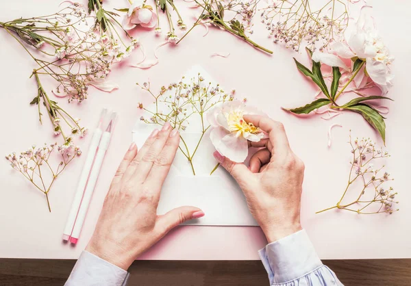 雌性的手做着可爱的花朵布置 花朵在打开的信封中 背景为淡粉色 顶部尽收眼底 富有创意的问候 邀请和假日概念 — 图库照片