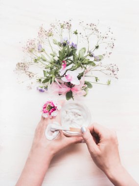 Kadın Eller, bitki dermatolojisi kozmetik kremini güzellik ve cilt bakımı için beyaz ahşap arka planda çiçekler ve otlarla kayganlaştırır. Botanik kozmetik ve güzellik konsepti