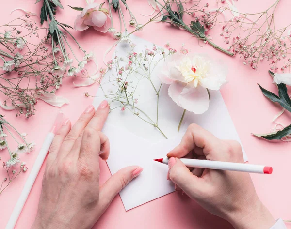 女性的手在信封上写着粉红桌子背景上的花朵 邀请函 情人节 母亲节问候和爱的概念 平面布局 顶视图 版权空间 — 图库照片