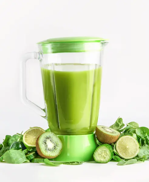 Blender with green smoothie with ingredients:  kiwi, cucumber, lime and spinach at white background. Preparing healthy juice. Front view.
