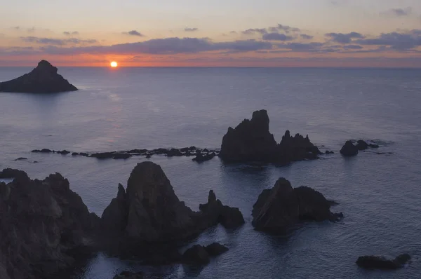 El sol saliendo del mar por el horizonte con rocas de un arrecife en primer plano