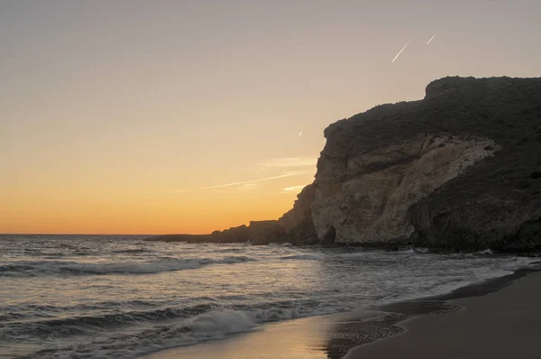 Puesta de sol en la playa con acantilados al fondo
