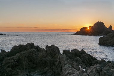 Sol ponindose tras las rocas en el mar