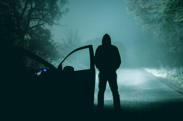 Samotny, zakapturzoną postać stojącą obok samochodu, patrząc na puste — Zdjęcie stockowe