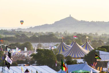 Haziran 25th 2011. Glastonbury Festivali. Glastonbury Festivali piramit aşamada arka plan ve Glastonbury Tor uzakta yüzen bir sıcak hava balonu ile. Güneşli bir akşam.