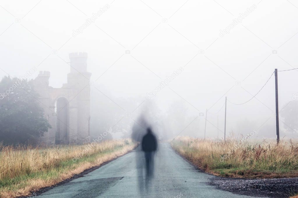 A lonely, ghostly silhouetted figure walking down a spooky, foggy lane next to the ruins of an old castle.