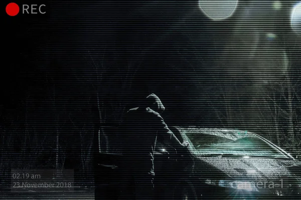 A threatening hooded man looking into a car at night. Photoshop edit to look like CCTV image.