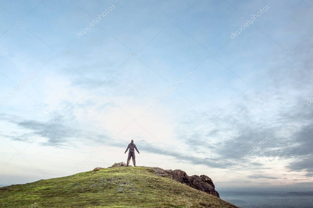 A man silhouetted against the sky with his arms outstrectched on top of a mountain. With copy space.