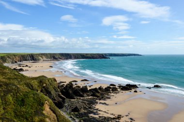 Bir vahşi engebeli plaj ve kıyı şeridi düşük tide, güneşli bir deve. İle kayalıklarla. Marloes Sands, Pembrokeshire. İngiltere.