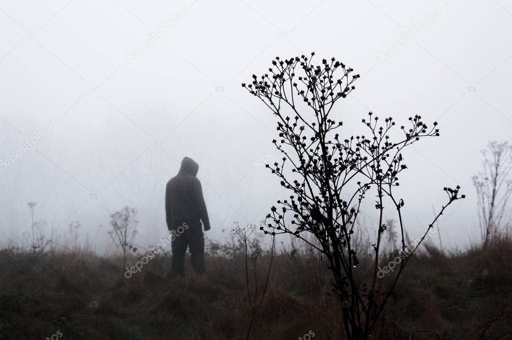 A moody out of focus hooded figure standing in the background on a foggy winters day. With a muted edit.