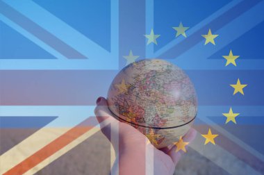 Brexit kavramı. Avrupa'da bir alana odaklanan bir küre tutan bir el. Union Jack ve E.U üzerinde bayrakları taşıyan üst üzerinde katmanlı. 