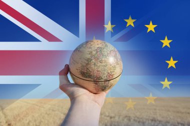 Brexit kavramı. Avrupa ve Afrika yaz buğday ve arpa alanında gösterilen bir küre tutan bir el. Union Jack ve E.U üzerinde bayrakları taşıyan üst üzerinde katmanlı. 