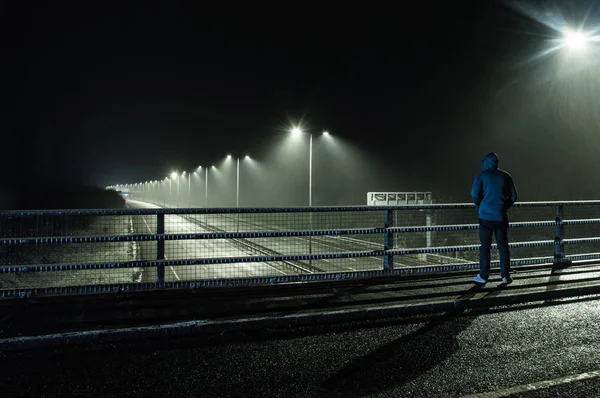 橋を見下ろして空高速道路で夜 吹雪の中に孤独なフード付き図立っています — ストック写真