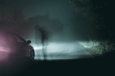 Bir hayalet kukuletalı şekil ayakta gece bir ürkütücü ülke yolda bir araba ile kontrast. Nezle grenli Düzenle.