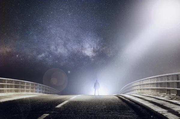 Uma figura sinistra com capuz silhada por luzes em uma estrada assustadora — Fotografia de Stock