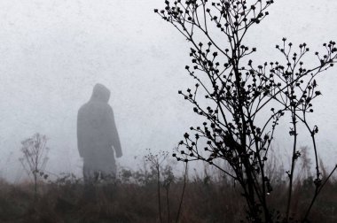 Sisli bir kış gününde arka planda duran odak kapüşonlu bir figür dışında bir huysuz hayalet. Sessiz grenli, grunge edit ile.