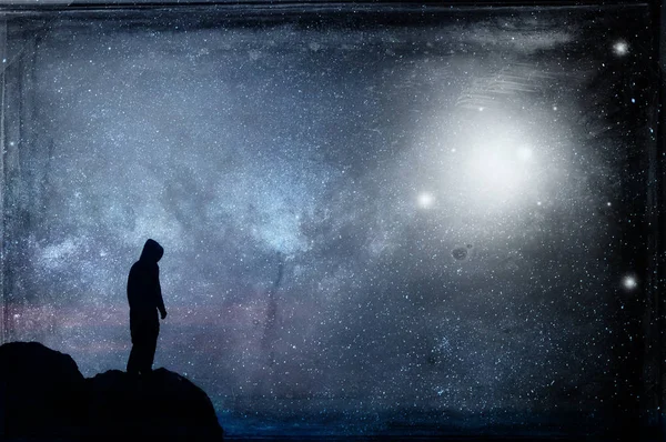 A lone hooded figure silhouetted, standing on a hill looking at a galaxy at night with UFOs floating in the sky. With a grunge, vintage edit.