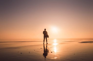 Bir adam Saunton, Devon, İngiltere'de batan güneşin karşı kontrast bir surfboard holding.