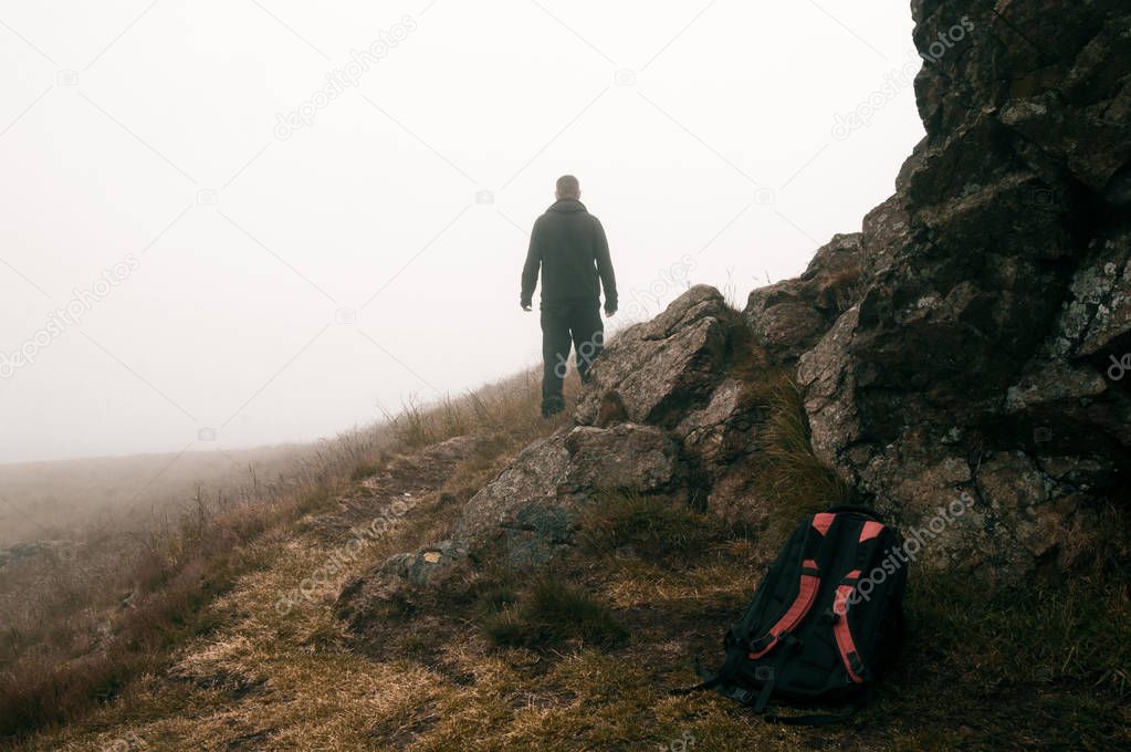 A lone hiker looking out into the mist on a bleak, spooky, foggy day in the hills.