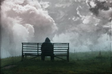 Gökyüzünde fırtına bulutları ile bir bankta oturan yalnız kapüşonlu bir adam, bir vintage, boyalı grunge edit ile